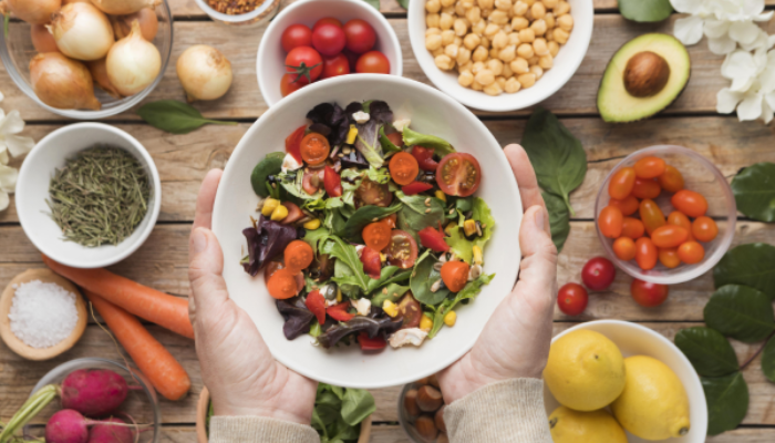 Fotografía para artículo topfarma sobre qué es una dieta equilibrada. Vemos una mesa llena de alimentos saludables y unas manos que sostienen un bol de ensalada variada y sana.